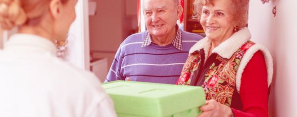 Frau übergibt Essensbox an älteres Ehepaar