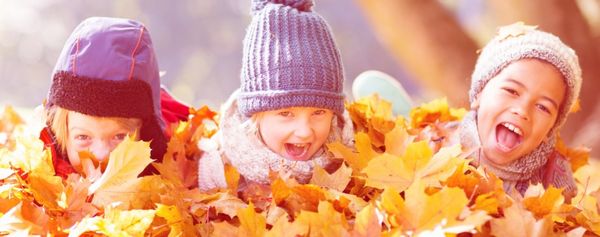 drei Kinder liegen im Herbstlaub