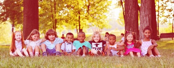 Mehrere Kinder sitzen im Gras unter Bäumen