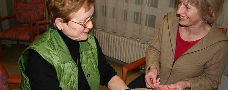 Besuchsdienst spielt Karten mit Pflegebedürftigen