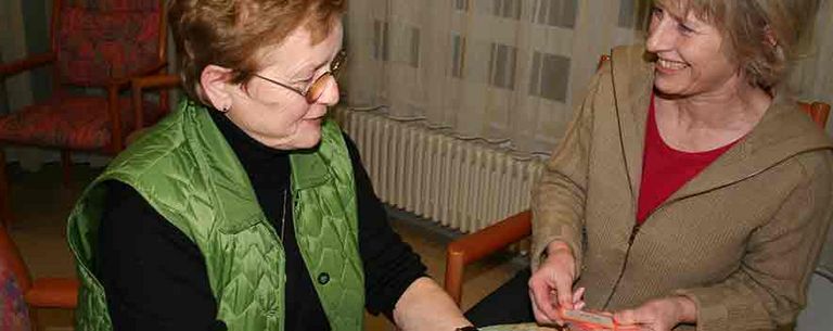 Besuchsdienst spielt Karten mit Pflegebedürftigen