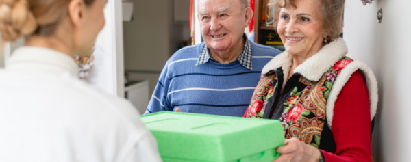Frau übergibt Essensbox an älteres Ehepaar